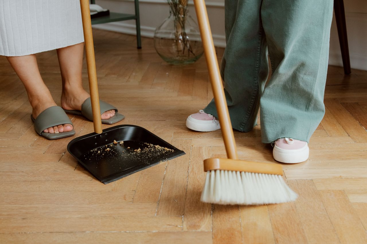 services-03 Close-up of people cleaning wooden floor with broom and dustpan indoors.